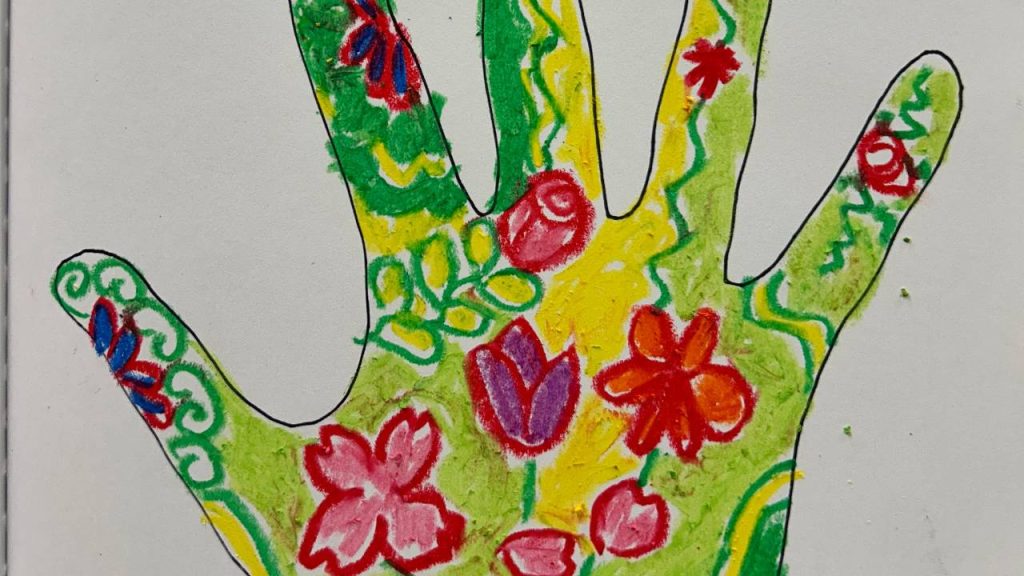 A hand outline is filled with colorful floral and swirl patterns in red, green, yellow, purple, and blue crayon on white paper.