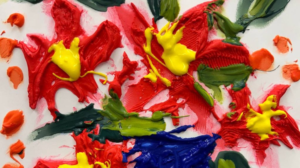 Thick smears of red, yellow, green, orange, and blue paint are layered and textured on white paper in a bold, expressive abstract artwork.